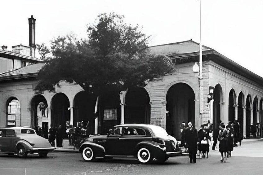 Ein Oldtimer, Fußgänger und ein Gebäude mit Rundbogenfenstern. 3