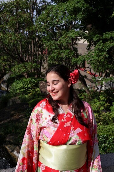 A person wearing a kimono with floral patterns, standing outdoors with trees and a building in the background. 2