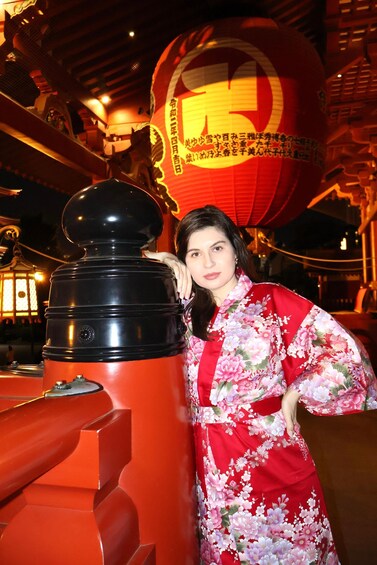 A person in a red floral dress standing next to a red and black structure with a spherical object in the background. 4