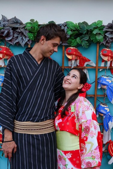 A person in a striped kimono and another in a floral kimono standing in front of a wall decorated with fish and leaves. 3
