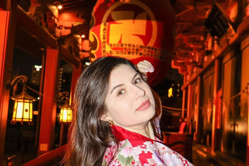 A person in a red floral garment standing in a traditional building with red lanterns and a large red circular emblem. 3