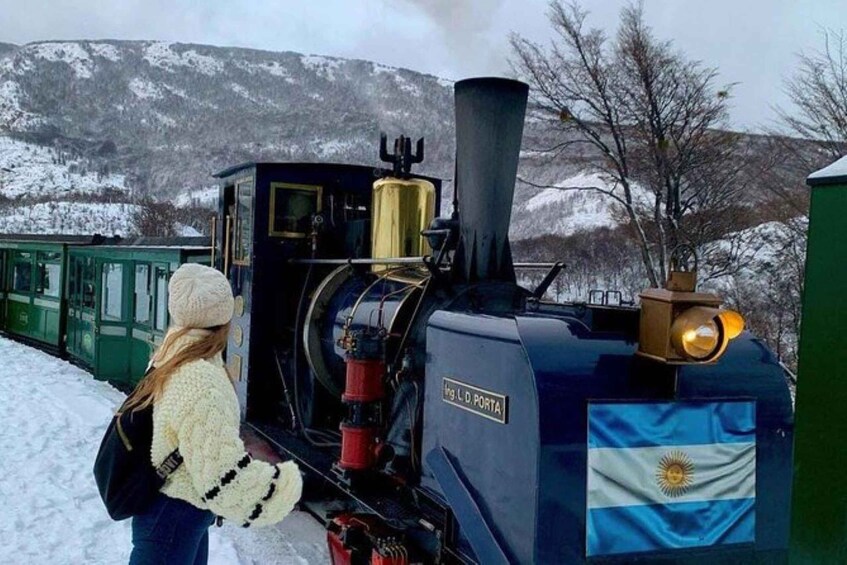 Een stoomlocomotief met een vlag, een persoon en besneeuwde heuvels op de achtergrond. 2