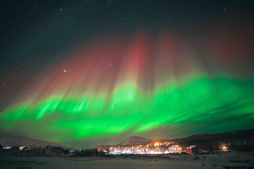 The Northern Lights over a snowy landscape with a town in the background. 1