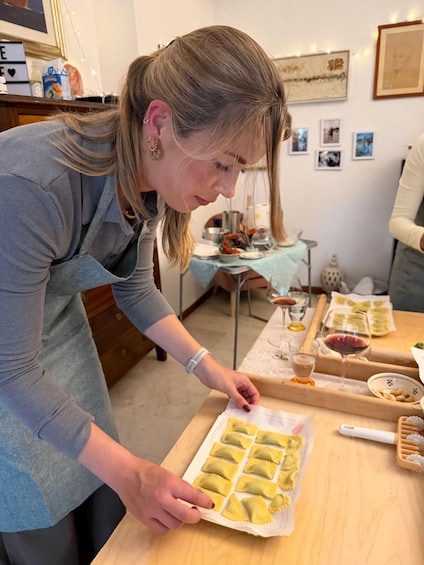 A person preparing food, specifically ravioli, on a wooden table with a blue tablecloth. 3