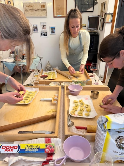 Three people making ravioli at a kitchen table with pasta ingredients and tools. 2