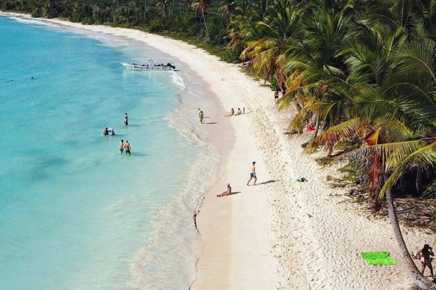 A beach with clear turquoise water, people swimming and walking along the shore, and palm trees lining the beach. 2