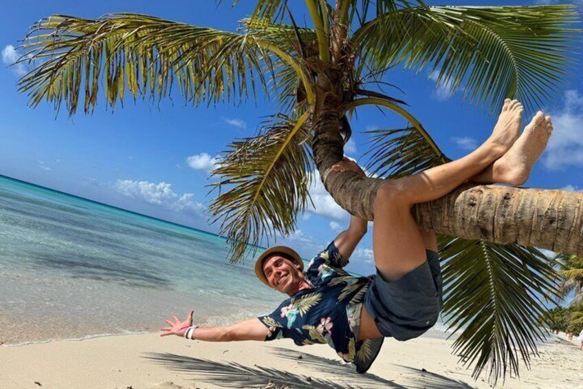 A person lying under a palm tree on a beach with clear blue water in the background. 1