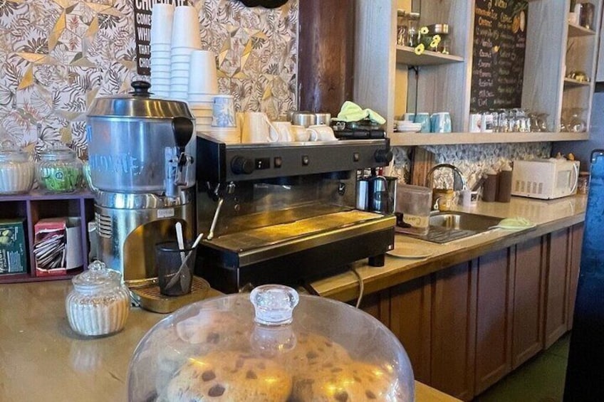 A coffee shop counter with a coffee machine, a water dispenser, and a glass dome covering a bowl of fruit. 2