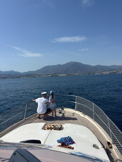 A boat with two people on deck, a mountainous landscape in the background, and calm water. 2