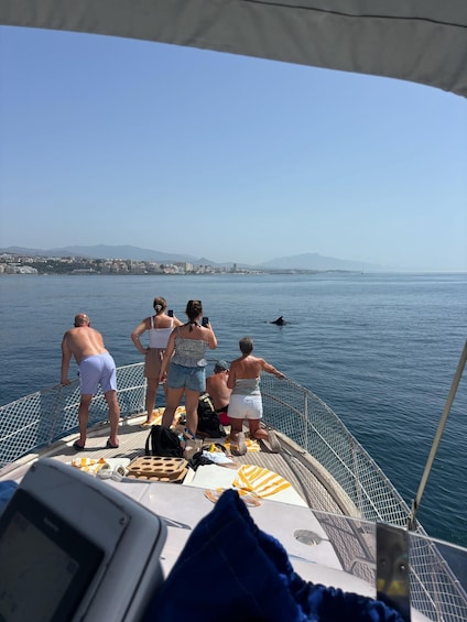 A group of people on a boat, looking out at the sea with a distant cityscape and mountains. 3
