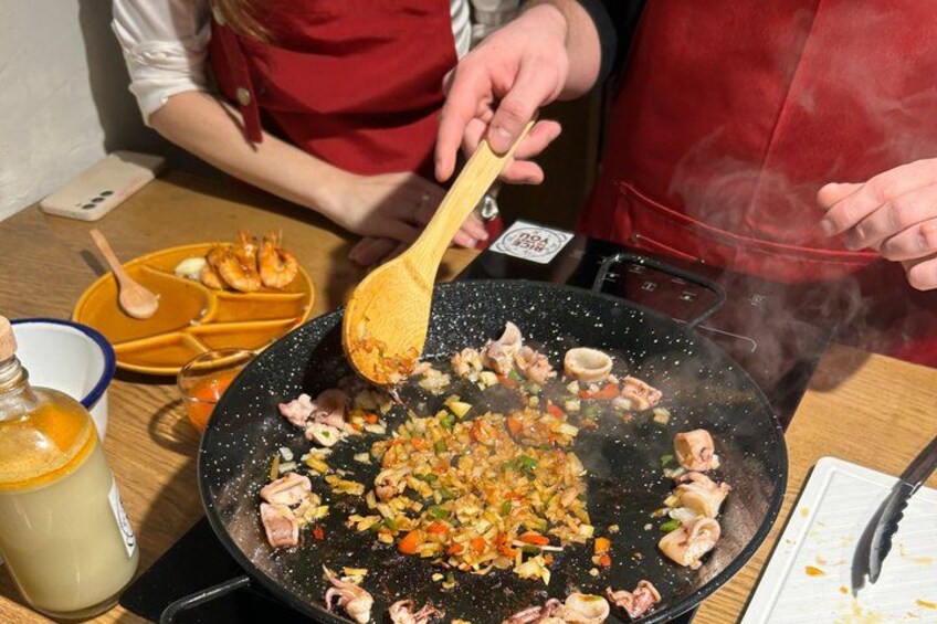 Eine Person kocht in einem Wok mit Gemüse und Fleisch, ein Handy und eine Tasse stehen auf dem Tisch. 3