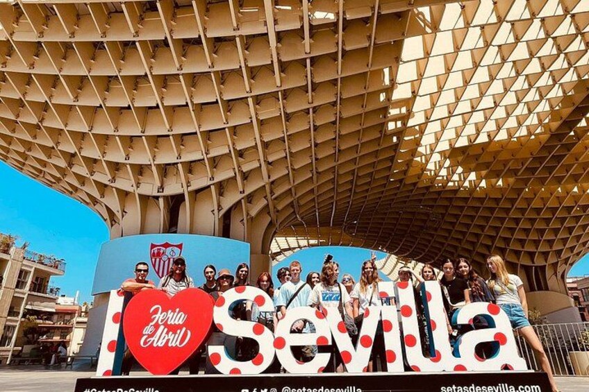 A group of people posing in front of a large sign with the text 'Sevilla' and 'Feria de Abril' on it. 1