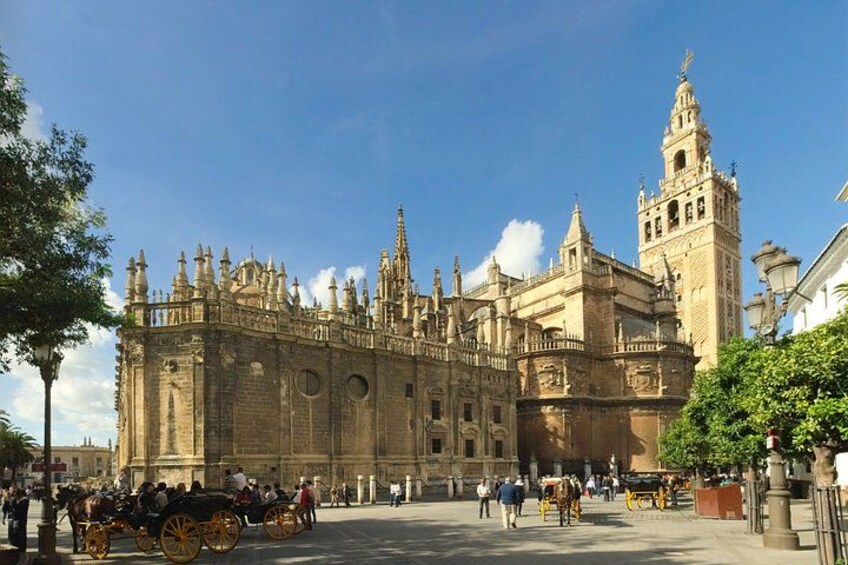 A historic building with intricate architecture, a prominent tower, and a plaza with people and horse-drawn carriages. 4
