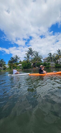 Two people kayaking on a calm river with palm trees and houses in the background. 3