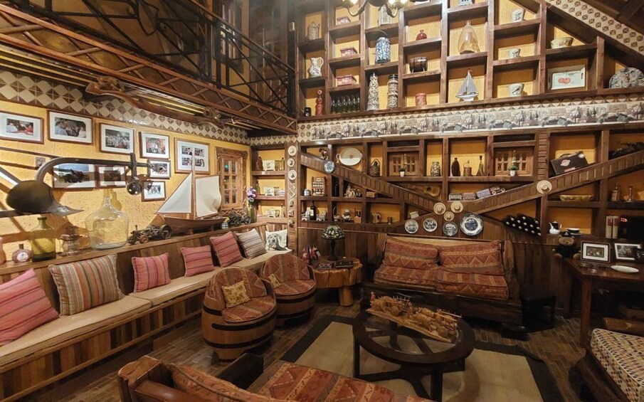 A cozy, vintage-style room with wooden furniture, shelves filled with decorative items, and a staircase. 3