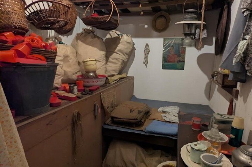 A cluttered room with a bed, a table with various items, and hanging baskets. 4