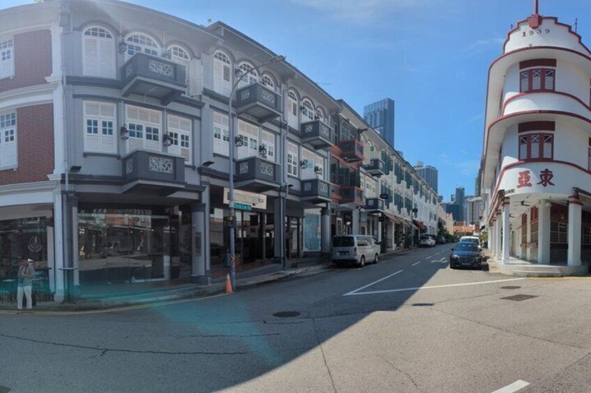 A street lined with multi-story buildings, some with commercial storefronts, and a distinctive white building with red signage on the right. 5