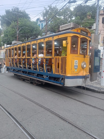 A yellow tram with passengers, on tracks, in an urban setting with buildings and trees. 2
