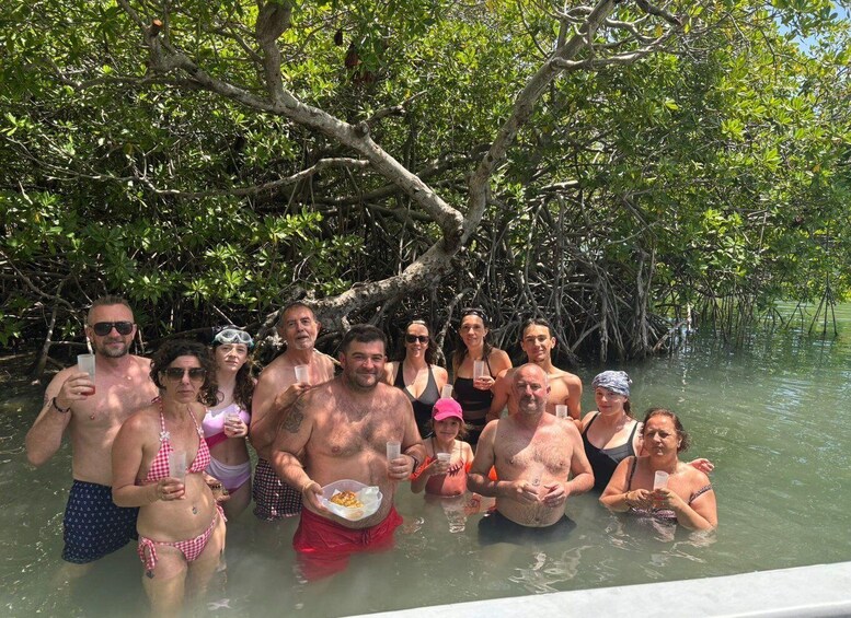 A group of people in a mangrove forest, some holding drinks and others with food. 4