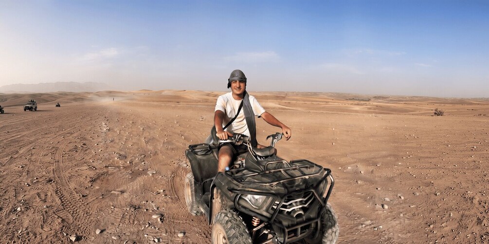 A person riding an ATV in a desert landscape with sand dunes and sparse vegetation. 3