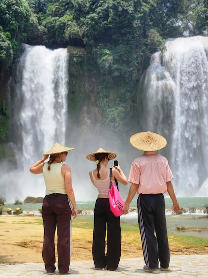 Three people standing in front of a waterfall, wearing hats, with one person taking a photo. 4