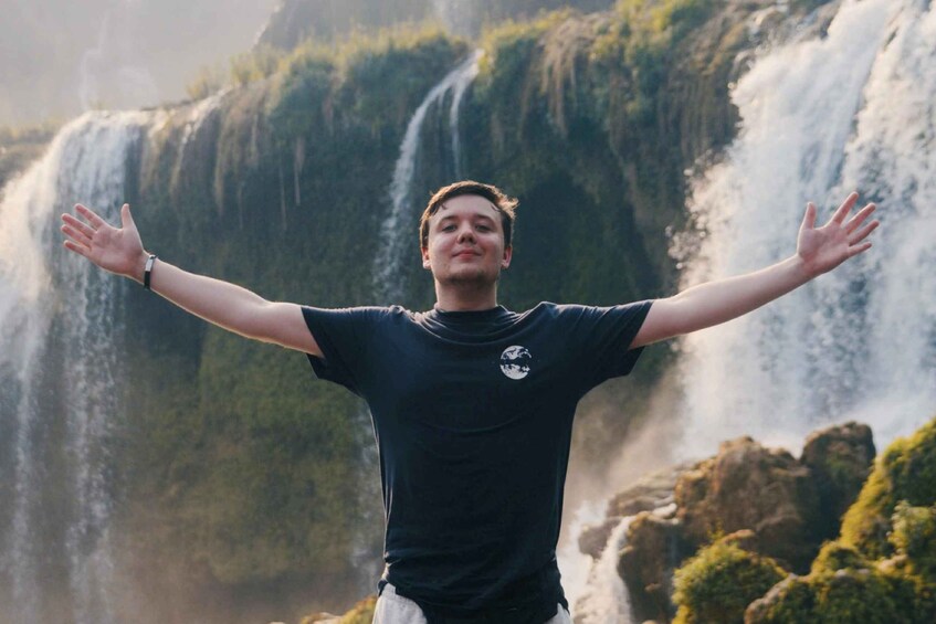 A person with arms outstretched in front of a waterfall. 1