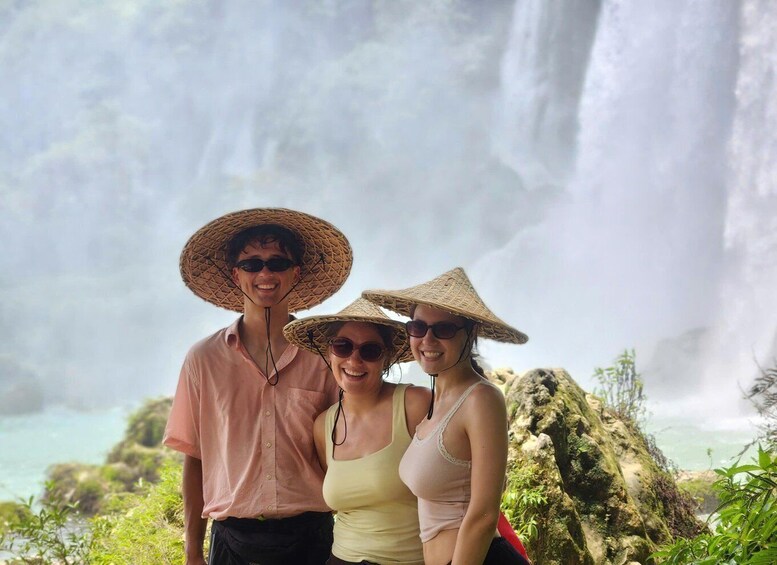 Three people standing in front of a waterfall with lush greenery in the background. 4