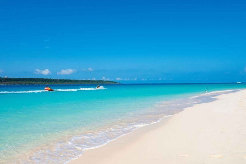 A beach with clear turquoise water, a sandy shore, and a distant shoreline with vegetation. 1