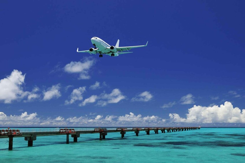 An airplane flying over turquoise waters with a pier extending into the sea. 1