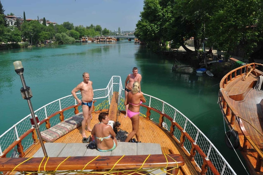 A boat with people on deck, a wooden railing, and a calm river. 5