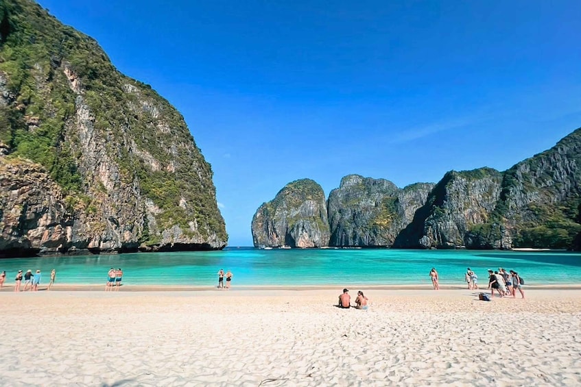 A beach with clear turquoise water, rocky cliffs, and people sunbathing. 4