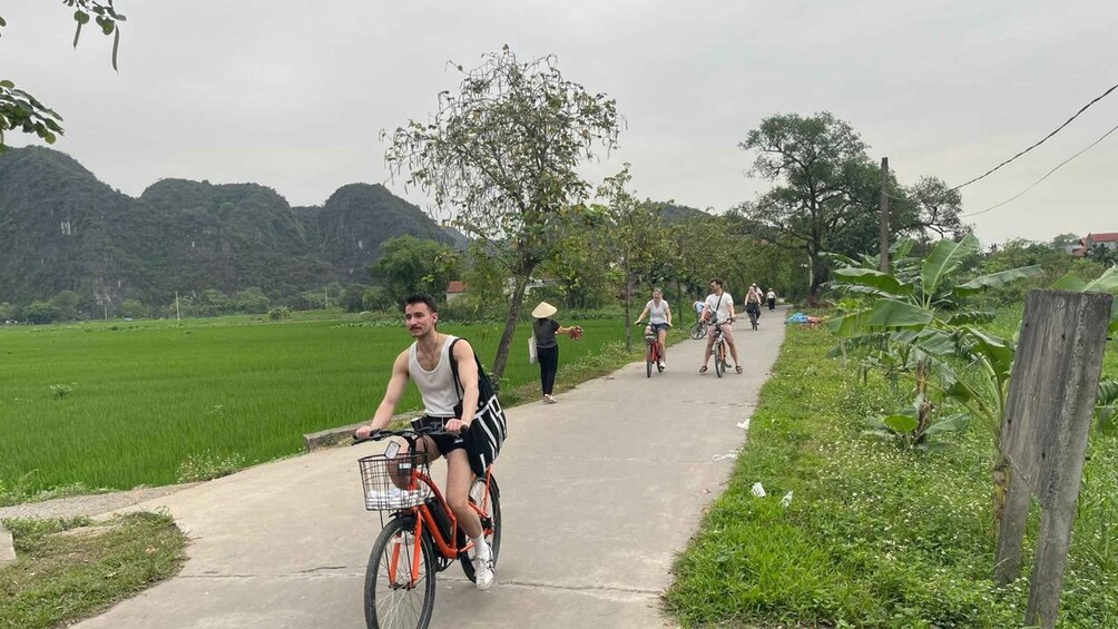 A paved path with cyclists and a person walking, surrounded by greenery and hills. 2