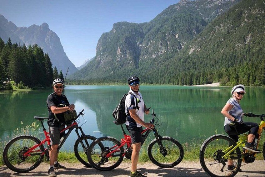 Three cyclists standing by a lake with mountains in the background. 5