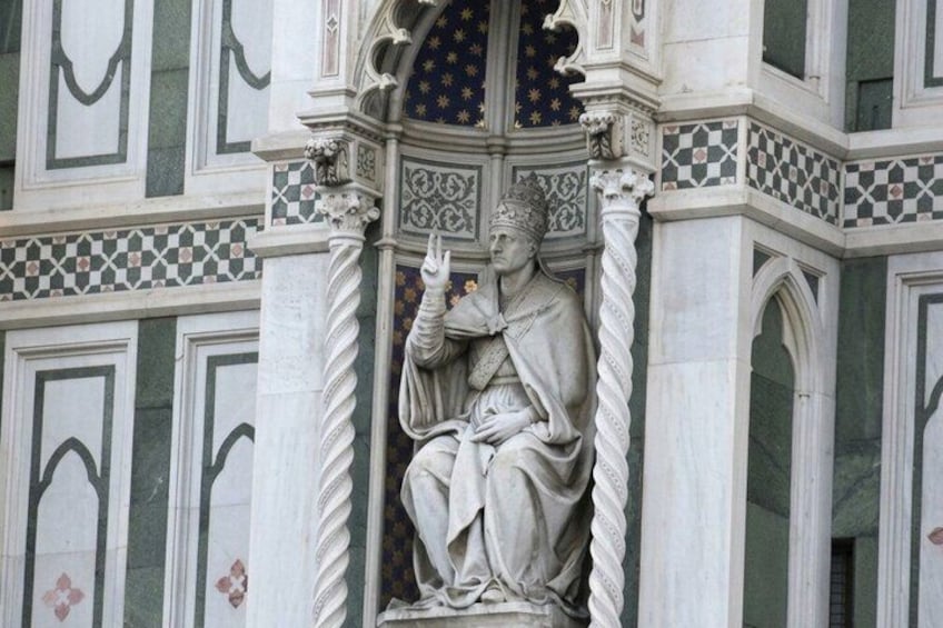 Een standbeeld van een beklede figuur met een halo, voor een muur met geometrische patronen. 4