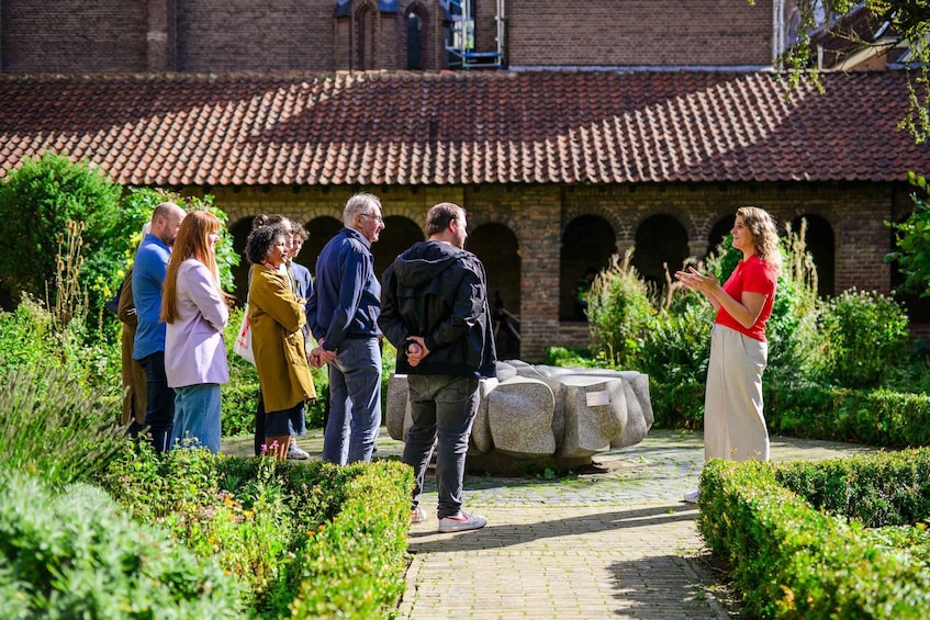 A group of people standing in a garden with a brick building in the background. 1