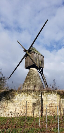 A windmill with a conical base and a wooden structure, set against a cloudy sky. 2