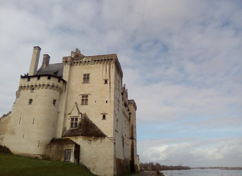 A historic castle with a round tower, a small annex, and a river in the background. 5