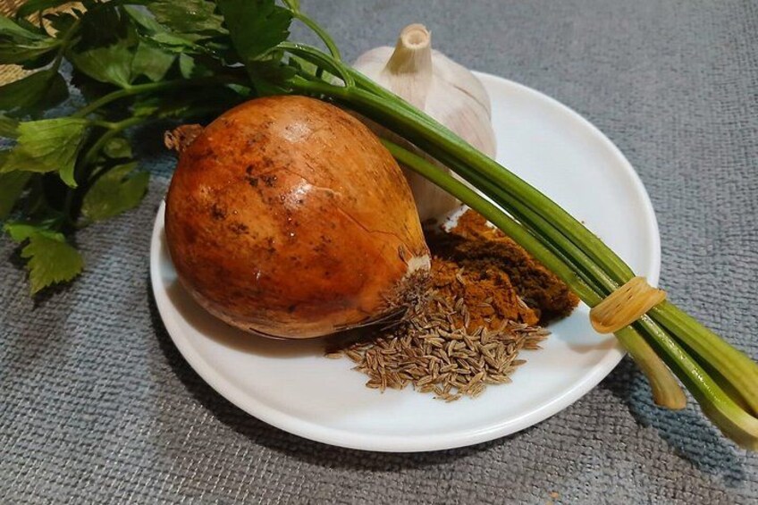 A white plate with a bulb, green onions, and cumin seeds. 2