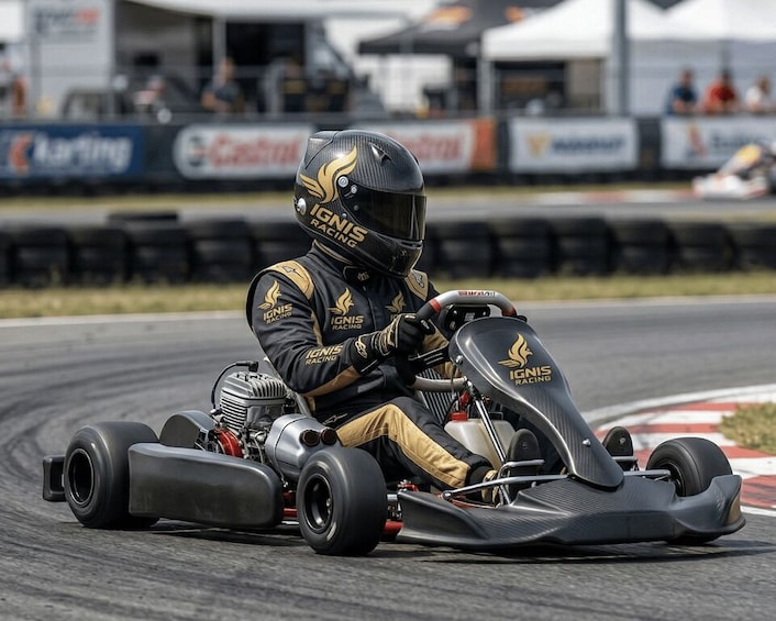 A go-kart racer in black and gold gear on a race track. 1