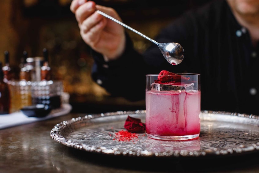 A cocktail with a pink hue, garnished with a red fruit, on a silver tray. 2