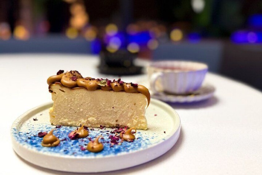 A slice of cheesecake on a plate with a blue pattern, accompanied by a cup of tea. 5
