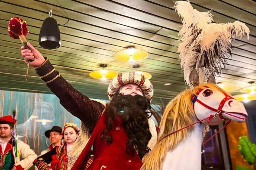 A person in traditional attire holding a red object, a horse with a white and red bridle, and a person in a green hat. 4