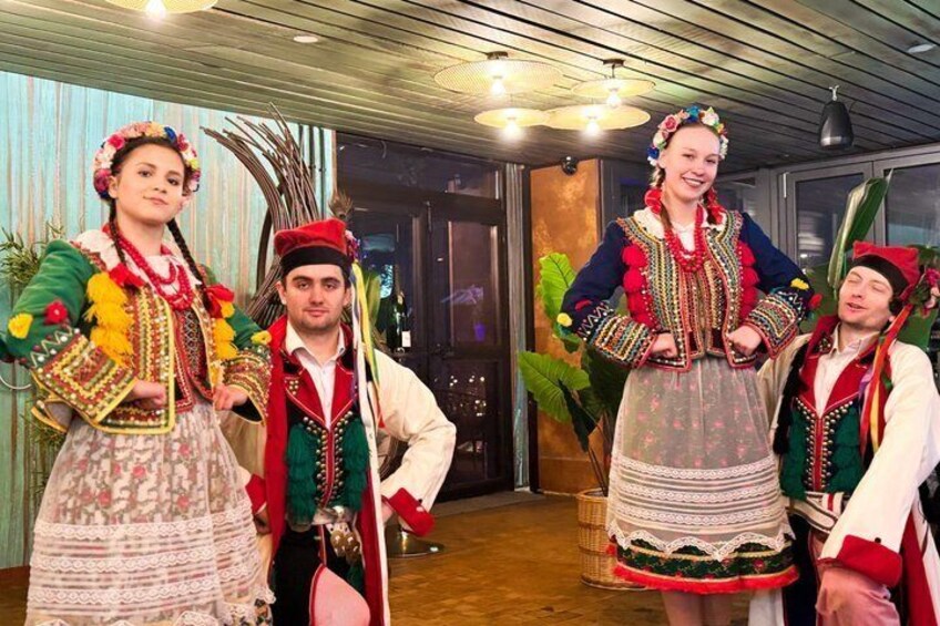 People in traditional costumes, a wooden ceiling, and indoor plants. 3