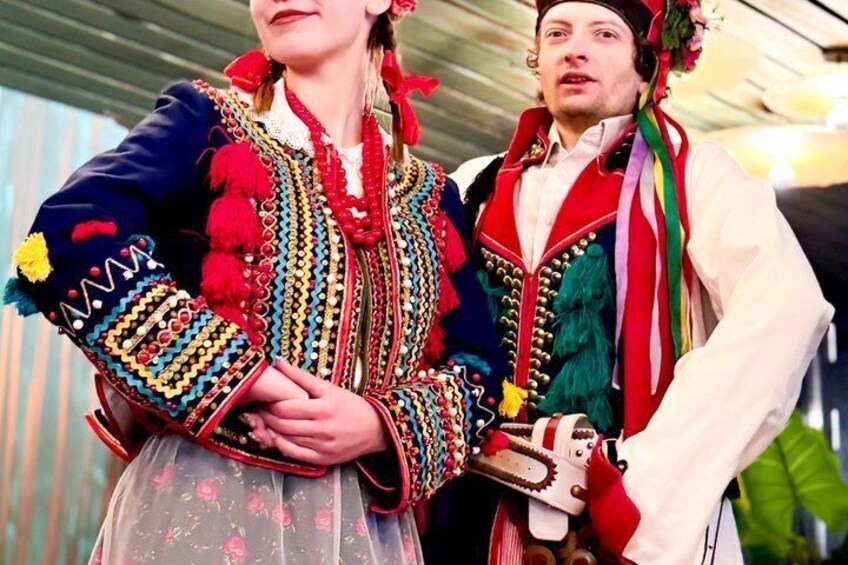 A person in traditional attire with colorful embroidery and a floral skirt. 1