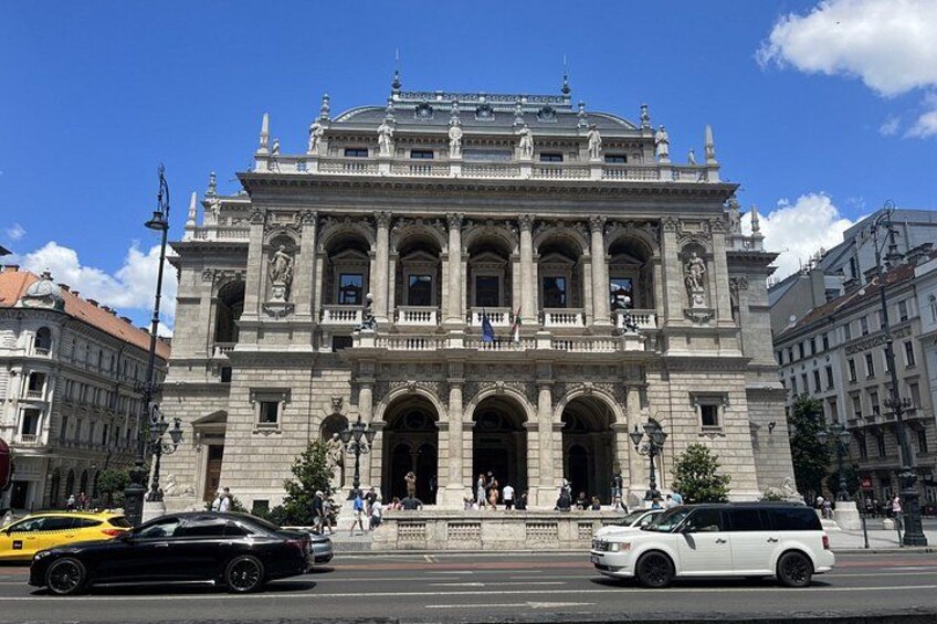 A historic building with ornate architecture, a large arched entrance, and a statue in front. 4