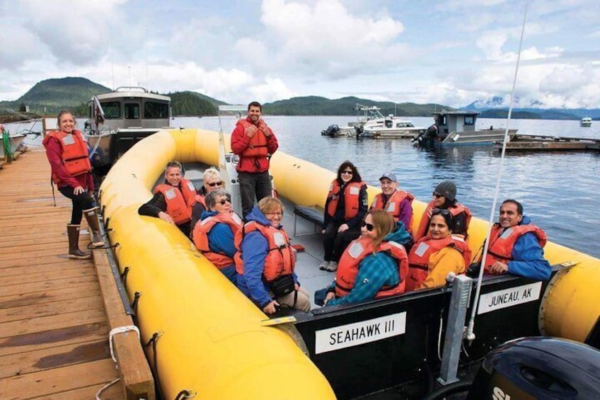 Eine Gruppe von Personen in einem gelben Schlauchboot mit Schwimmwesten liegt an einem Jachthafen fest, im Hintergrund sind Boote und Hügel zu sehen. 3