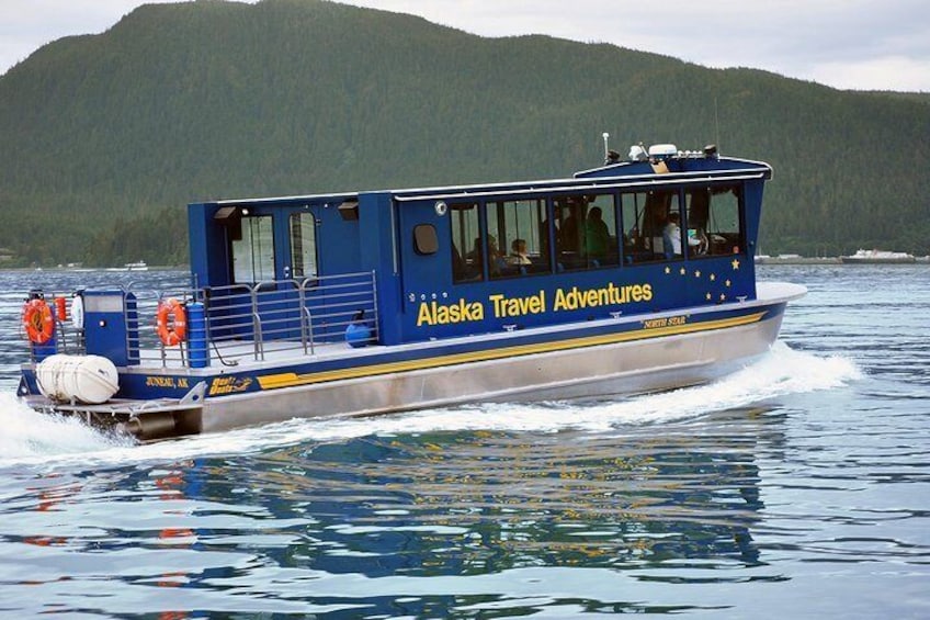 A blue boat with 'Alaska Travel Adventures' written on the side, moving on water with a forested hill in the background. 4