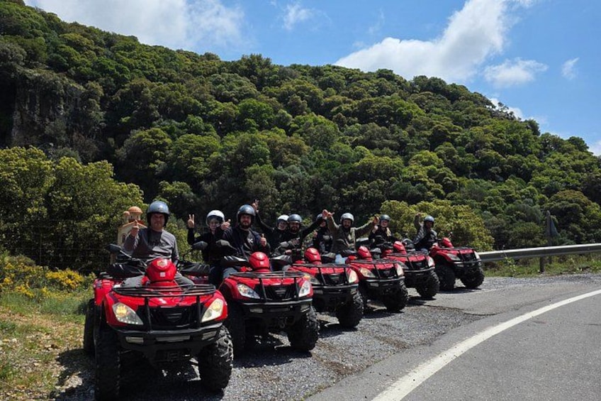 A group of people on red ATVs on a road with a forested hill in the background. 1