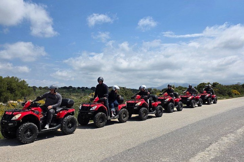 A group of people riding red quad bikes on a paved road with a clear sky. 5