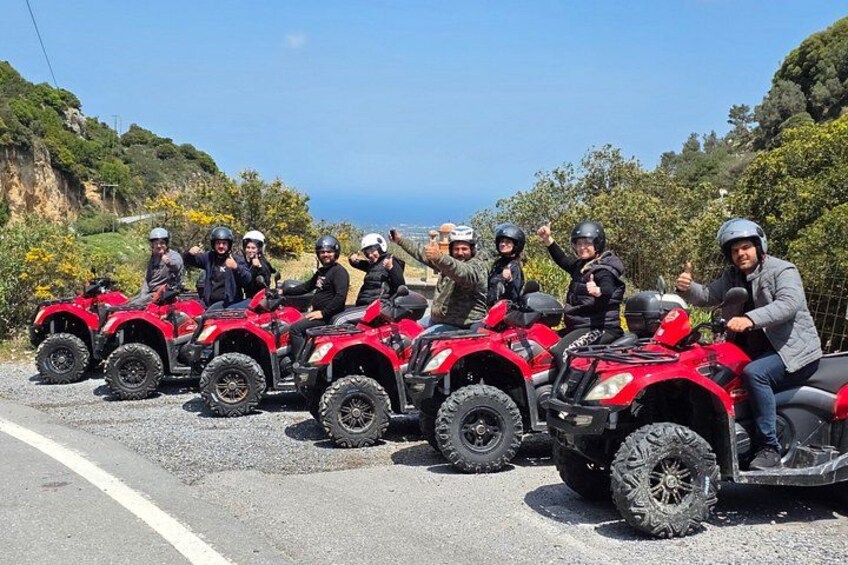 A group of people on red quad bikes on a road with a coastal landscape in the background. 2